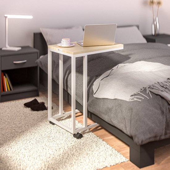 Bijzettafel met lichtbruin houten blad en wit metalen frame, naast een bed.