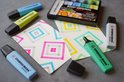Blauwe, gele en groene STABILO BOSS markers op papieren met geometrische patronen.