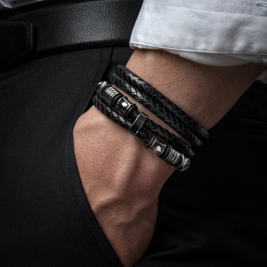 Gevlochten zwarte armband met zilverkleurige buisjes en ringen, gedragen op de pols van een man.