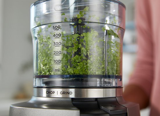 Close-up van een Kenwood chopper met fijngehakte kruiden, tot 500 ml.