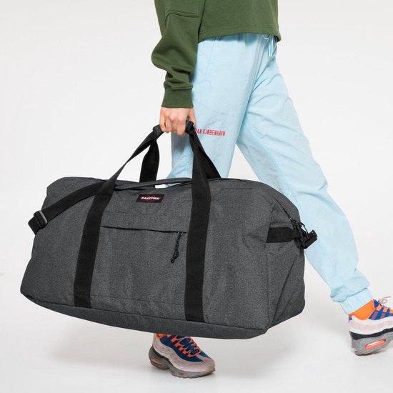 Persoon die een donkergrijze Eastpak reistas draagt met een band over de schouder.