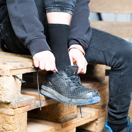 Man met zwarte werksokken strikt blauw-zwarte werkschoenen