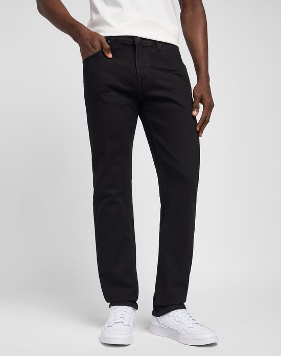 Man met zwarte jeans, staand van voren, met witte sneakers.