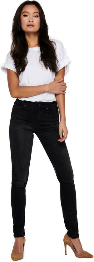 Model van voren gezien in een strakke zwarte jeans met hoge taille, witte top en bruine pumps.
