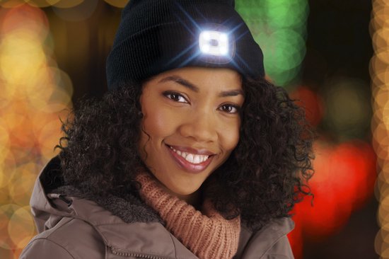 Zwarte beanie met een ingebouwde, verlichte lamp die fel wit licht geeft. Een lachende vrouw met krullend haar draagt de muts.
