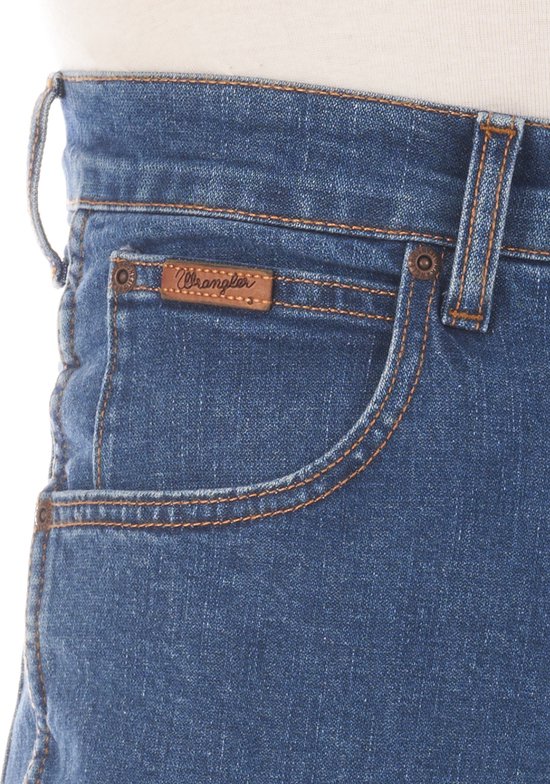 Detail van een blauwe Wrangler jeans, met bruin leren label op de voorkant.