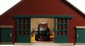 Binnenkant van een speelgoedboerderij met een groene tractor en rood-wit koeien.