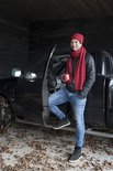 Een man met rode muts en sjaal staat naast een pick-up truck met een mok in zijn hand.