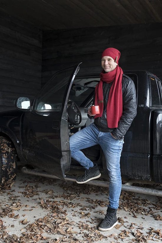 Een man met rode muts en sjaal staat naast een pick-up truck met een mok in zijn hand.