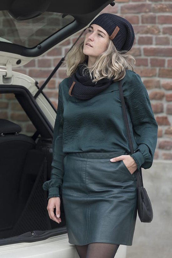 Een vrouw met een zwarte gebreide muts en sjaal, een donkergroene top en leren rok.