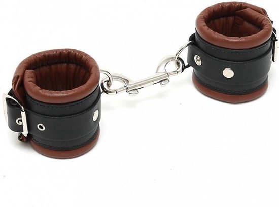 Zwart leren enkelboeien met bruine voering en gespen, verbonden door een metalen ketting met karabijnsluitingen.