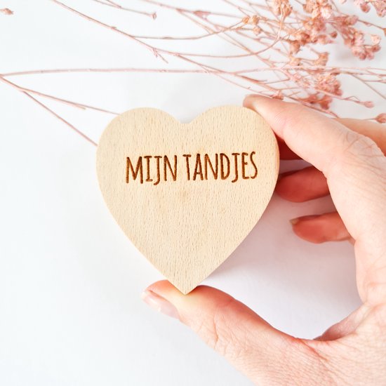 Hand die een houten hartvormig doosje vasthoudt met de tekst "MIJN TANDJES".