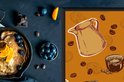 Close-up van een oranje kookplaatbeschermer met illustraties van koffiekannen.