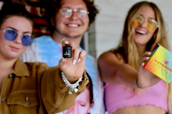 Drie jonge mensen met zonnebrillen, een van hen houdt een zwarte Eargasm oordoppen koker vast.