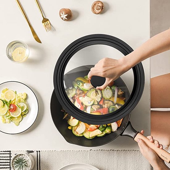 Hand die een zwart glazen deksel met siliconen rand op een wok met groenten plaatst.