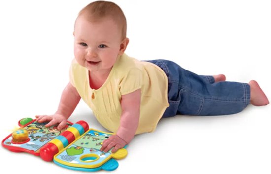 Baby in geel shirt en spijkerbroek ligt op de buik, spelend met het VTech Bumba Muziekboekje.