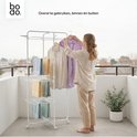Een vrouw hangt kleding aan een witte droogtoren met vier niveaus, op een balkon.