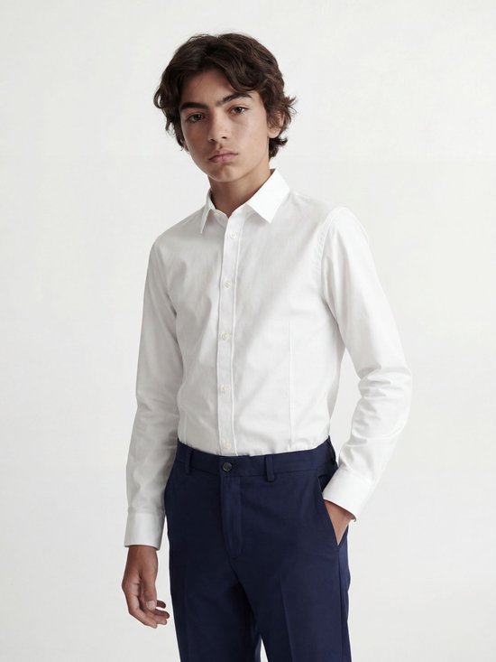 Un garçon porte une chemise blanche à manches longues et un pantalon bleu.
