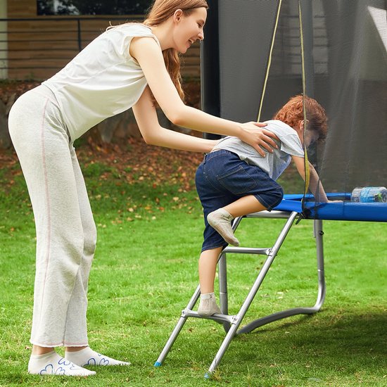 Moeder helpt een jong kind met een rode broek op de ladder van een blauwe trampoline te klimmen.