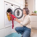 Vrouw met bril met rood warmtekussen naast een open wasmachine.