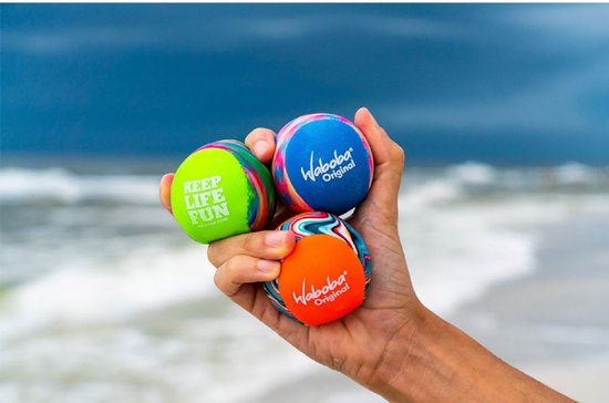 Hand houdt drie Waboba ballen vast: oranje, blauw en groen met "Keep Life Fun" tekst.