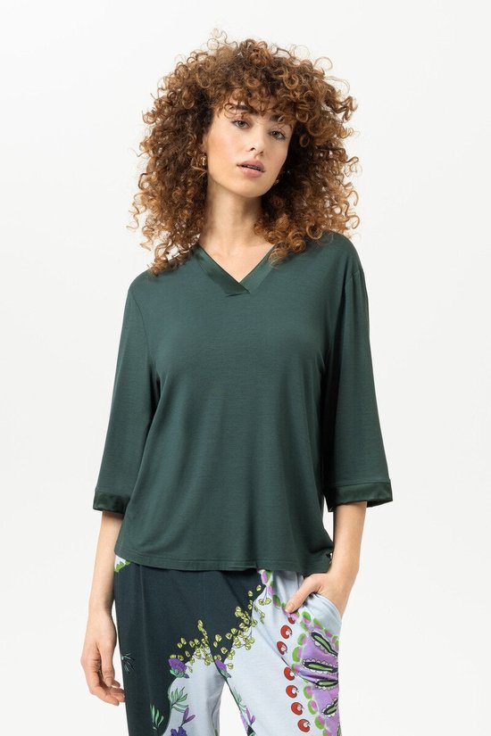 Donkergroen T-shirt met V-hals en driekwart mouwen, met satijnen boordjes. Gedragen met een broek met kleurrijke print.