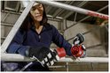 Vrouw in blauw werkpak en helm, op steiger, verbindt rode 5-polige CEE-stekker met koppeling.