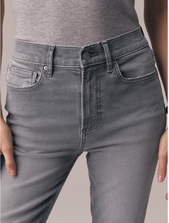 Close-up van de tailleband en zakken van een grijze jeans met een grijze top.