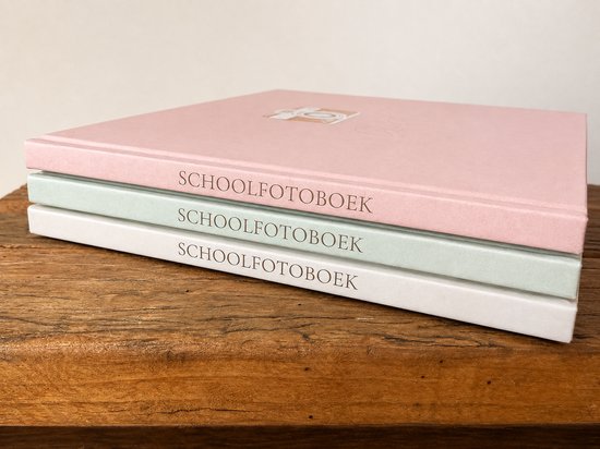Grijze, roze en lichtgroene schoolfotoboeken gestapeld op een houten plank. De boeken hebben gouden letters op de rug. De bovenste twee boeken hebben een blinddruk.