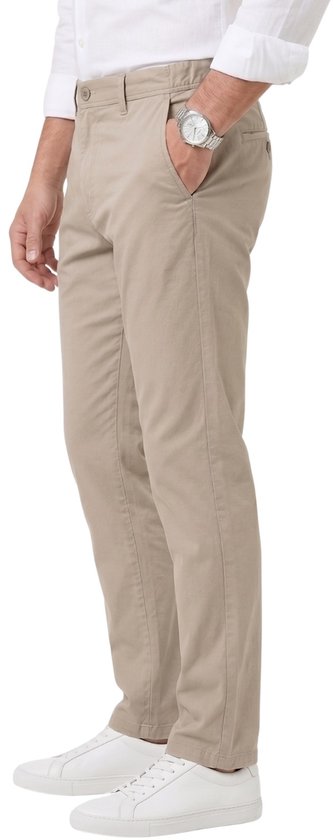 Zijaanzicht van een man met beige chino broek, witte blouse, horloge en witte sneakers, hand in zak.