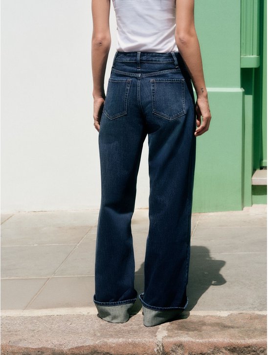 Achterkant van een model in donkerblauwe boyfriend jeans met omgeslagen pijpen.