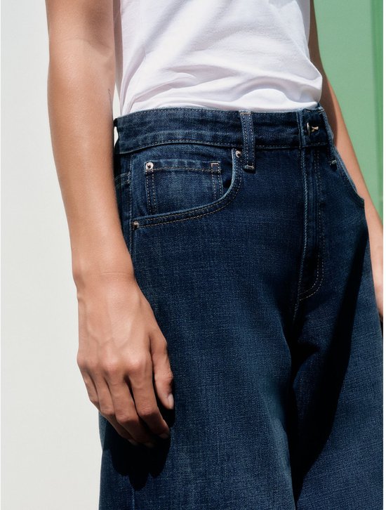 Close-up van de tailleband van een donkerblauwe boyfriend jeans.