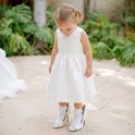 Een jong meisje met staartjes in een witte jurk, draagt een te grote witte pumps met witte sokjes met kanten randjes.