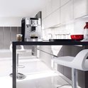 Zilveren De'Longhi Magnifica S espressomachine in een moderne keuken, met twee kopjes espresso en cappuccino ernaast.