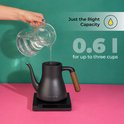 Hand vult zwarte CHiATO waterkoker met hout handvat met water uit glazen karaf. Capaciteit 0.6 l.