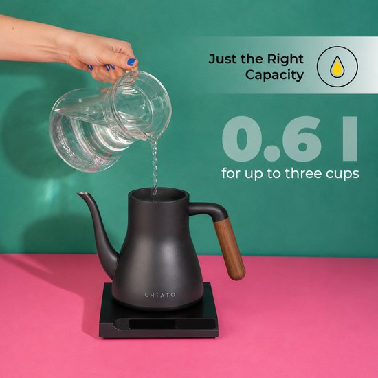 Hand vult zwarte CHiATO waterkoker met hout handvat met water uit glazen karaf. Capaciteit 0.6 l.