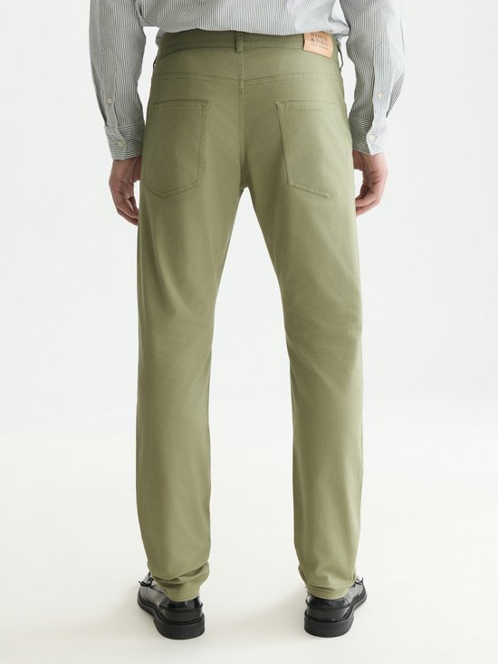 Achterkant van een man in een olijfgroene chino met een gestreept overhemd en zwarte schoenen.