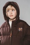 Gedetailleerde close-up van een kind in een bruine pufferjas met zichtbaar "Moodstreet" logo.