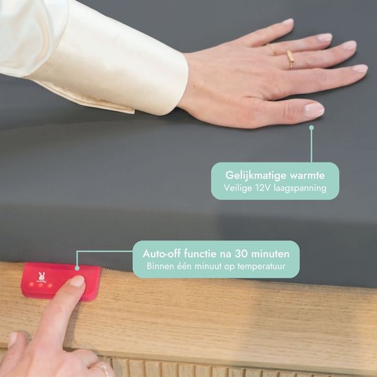 Een hand met ringen raakt een grijs oppervlak aan. Een rode Wumby oplader met een roze knop. 'Gelijkmatige warmte' en 'Auto-off functie na 30 minuten'.