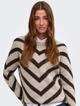 Model draagt een beige trui met bruine chevronprint, een witte blouse eronder.