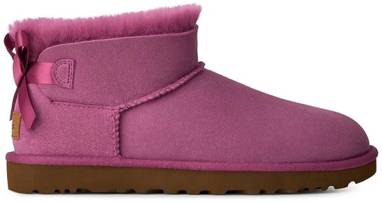 Paarse UGG-enkelboot met suède, harige kraag, roze strik aan de achterkant en platte bruine rubberen zool.
