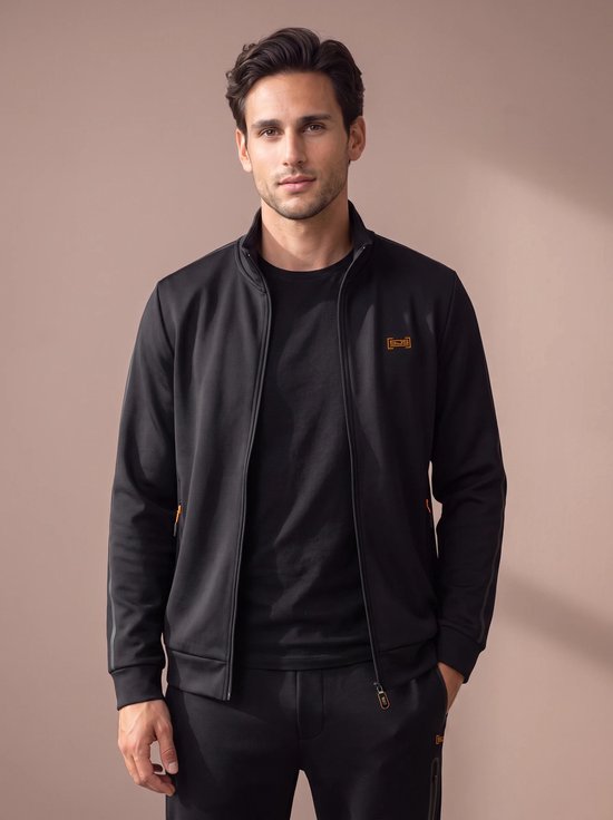 Model draagt een zwart sportvest met oranje accenten en een klein oranje logo op de borst.