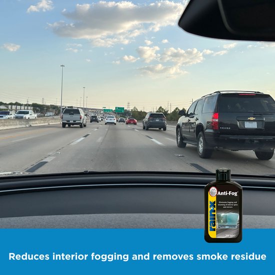 Autoruit zicht van binnenuit op snelweg. Fles Rain-X Anti-Fog rechtsonder. Tekst 'Reduces interior fogging'.