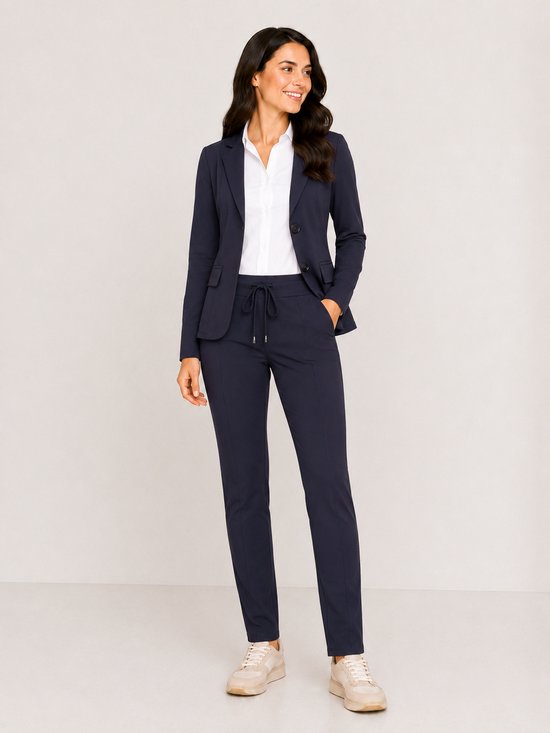 Vrouw in marineblauw pak van Mi Piace, met blazer en broek. De blazer is aan de voorkant te zien, met witte blouse en sneakers.