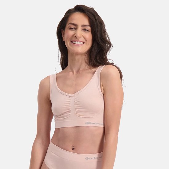Een lachende vrouw in een lichtroze naadloze BH van Bamboo Basics. De BH heeft een V-hals en ruches in het midden.