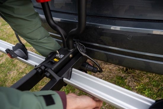 Detailopname van de bevestiging van een trekhaakfietsendrager aan een auto, met kabelaansluitingen.