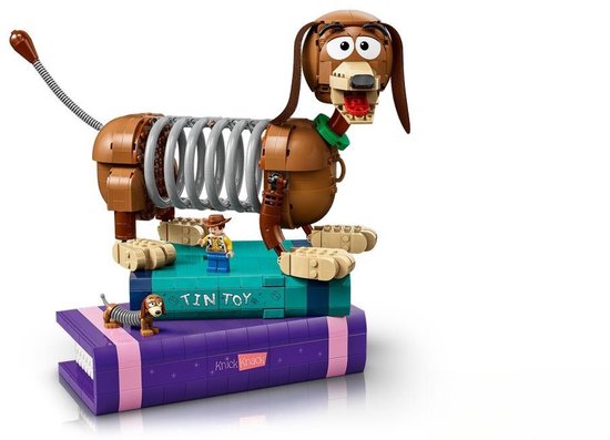 LEGO Slinky Hond opgestapeld op paarse en blauwe LEGO boeken met Woody en een kleine hond.