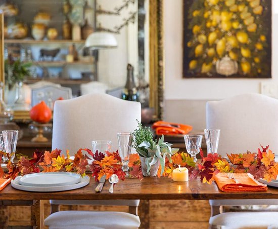 Herfstbladerenslinger op een houten eettafel met servies.