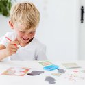 Jeune garçon aux cheveux blonds, souriant, assis à une table avec un kit de peinture diamant sur le thème du Grinch.