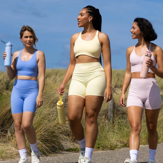 Drie vrouwen lopen buiten, elk met een gekleurde CABAU waterfles. Van links naar rechts: lichtblauw, geel, roze.